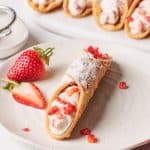 A Strawberry Cannoli on a white plate next to a platter of more.