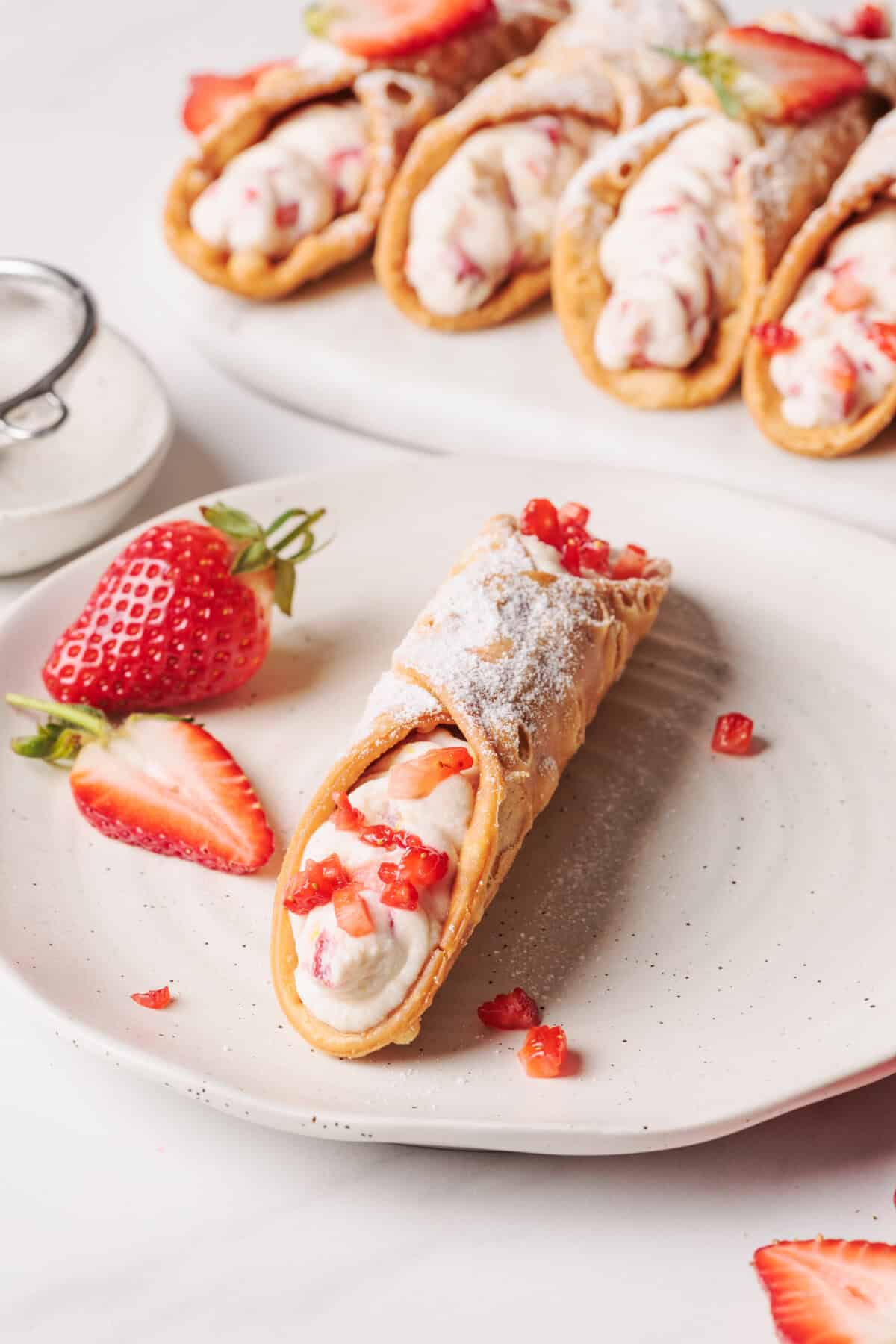 A Strawberry Cannoli on a white plate next to a platter of more.