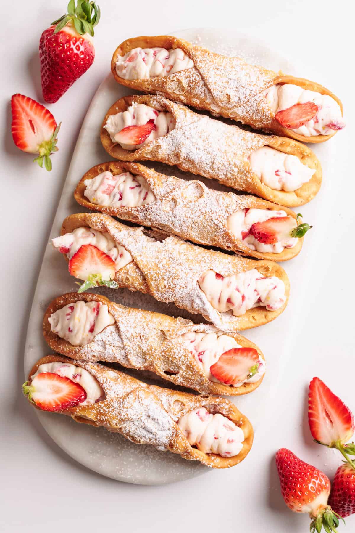 A marble platter with six Strawberry Cannoli.
