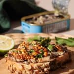 Sardines on toast on a wooden board next to a tin.