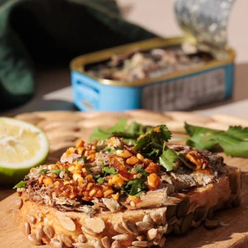Sardines on toast on a wooden board next to a tin.