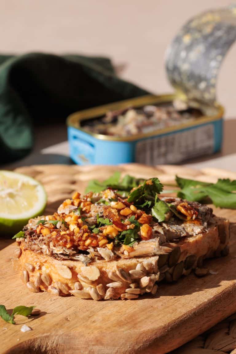 Sardines on toast on a wooden board next to a tin.