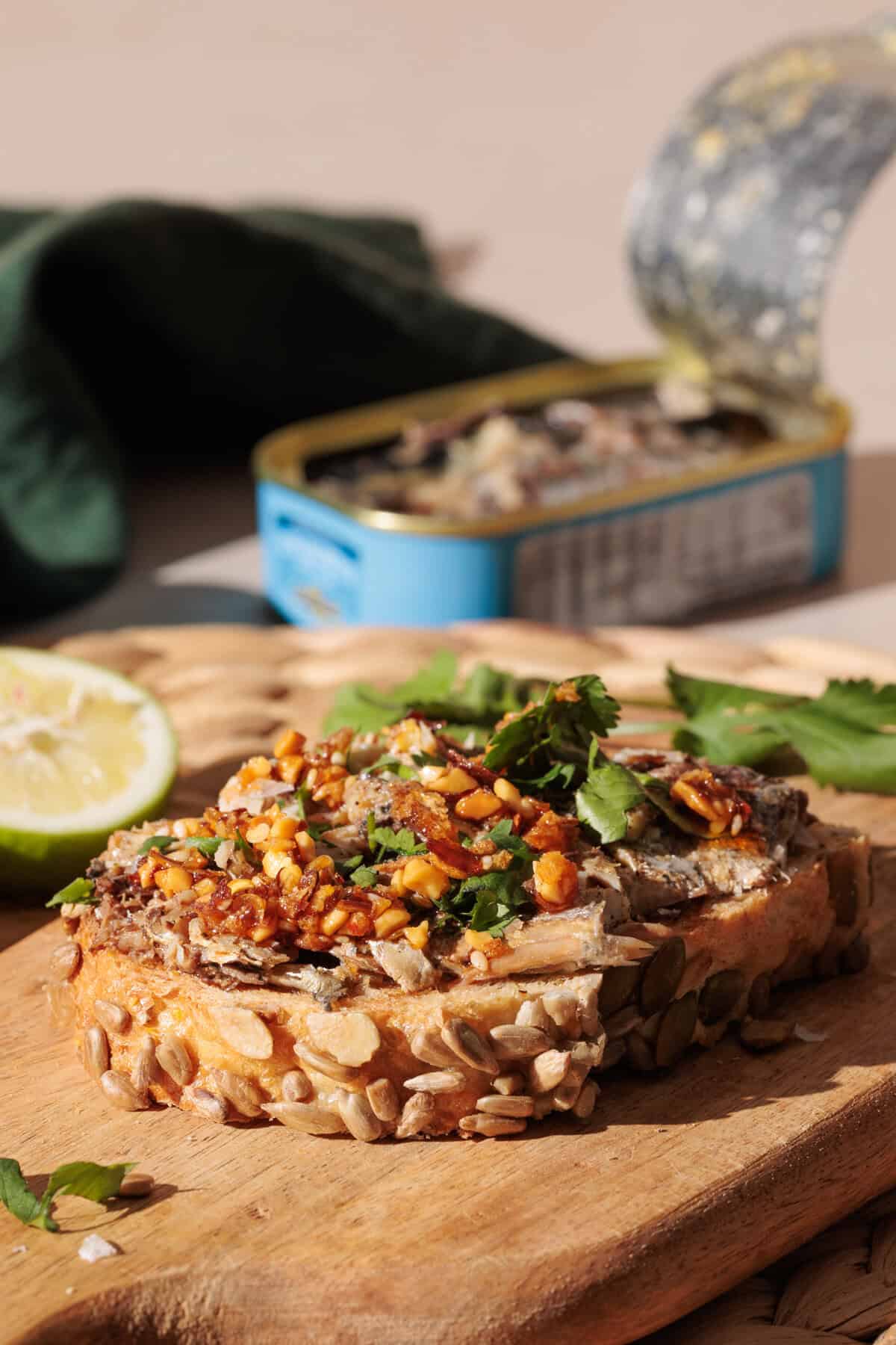 Sardines on toast on a wooden board next to a tin.