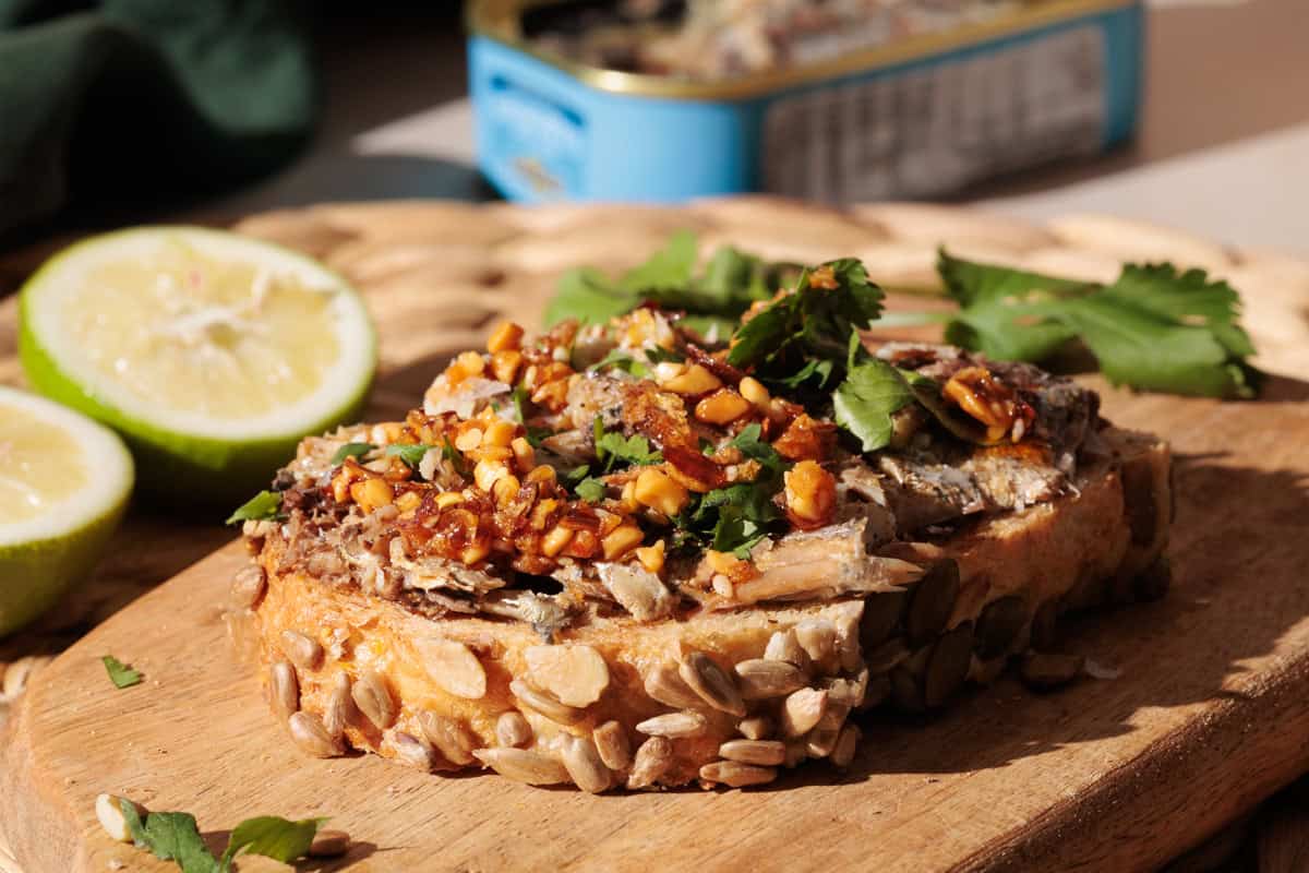 Sardines on toast on a wooden board next to a tin.